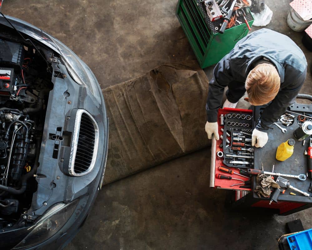 A man repairs a car in a garage, highlighting the convenience of mobile mechanics over traditional shops.